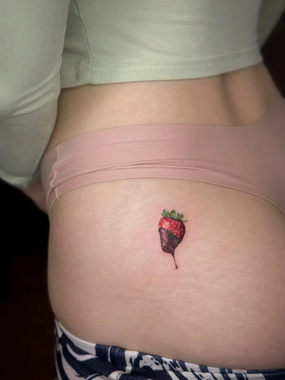 Tatuaj color pe șold cu o căpșună înmuiată în ciocolată neagră