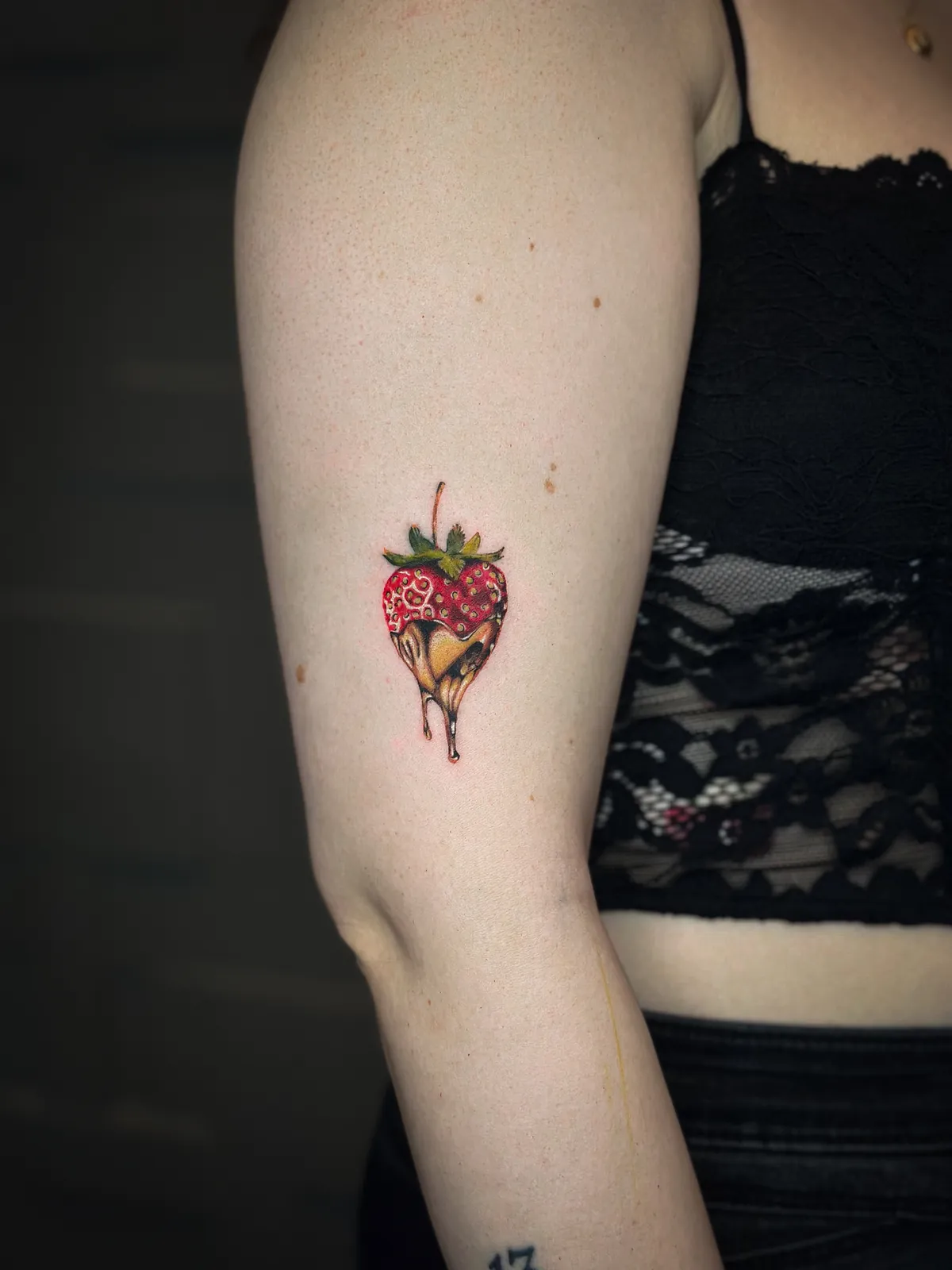 Tatuaj color pe braț cu o căpșună în formă de inimă, înmuiată în ciocolată neagră
