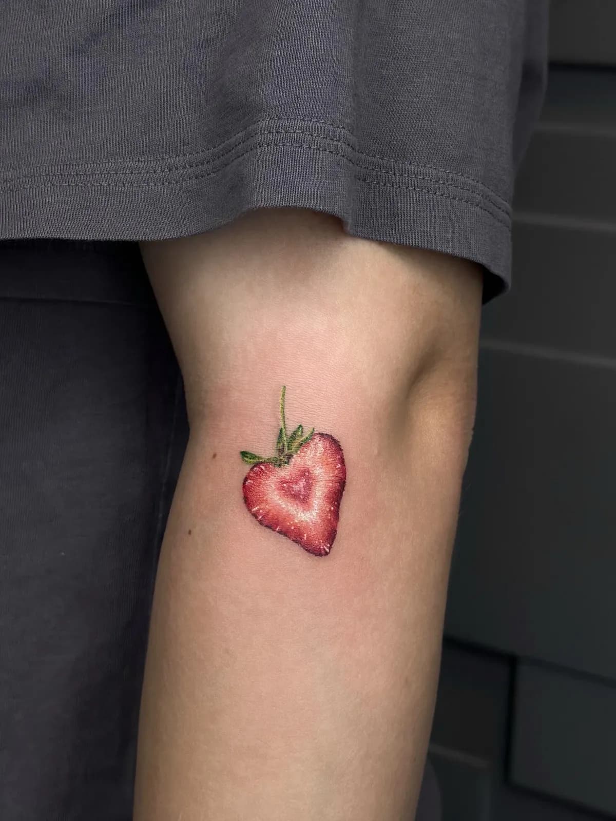 Tatuaj color pe braț cu o căpșună tăiată, cu o inimă mică în interior
