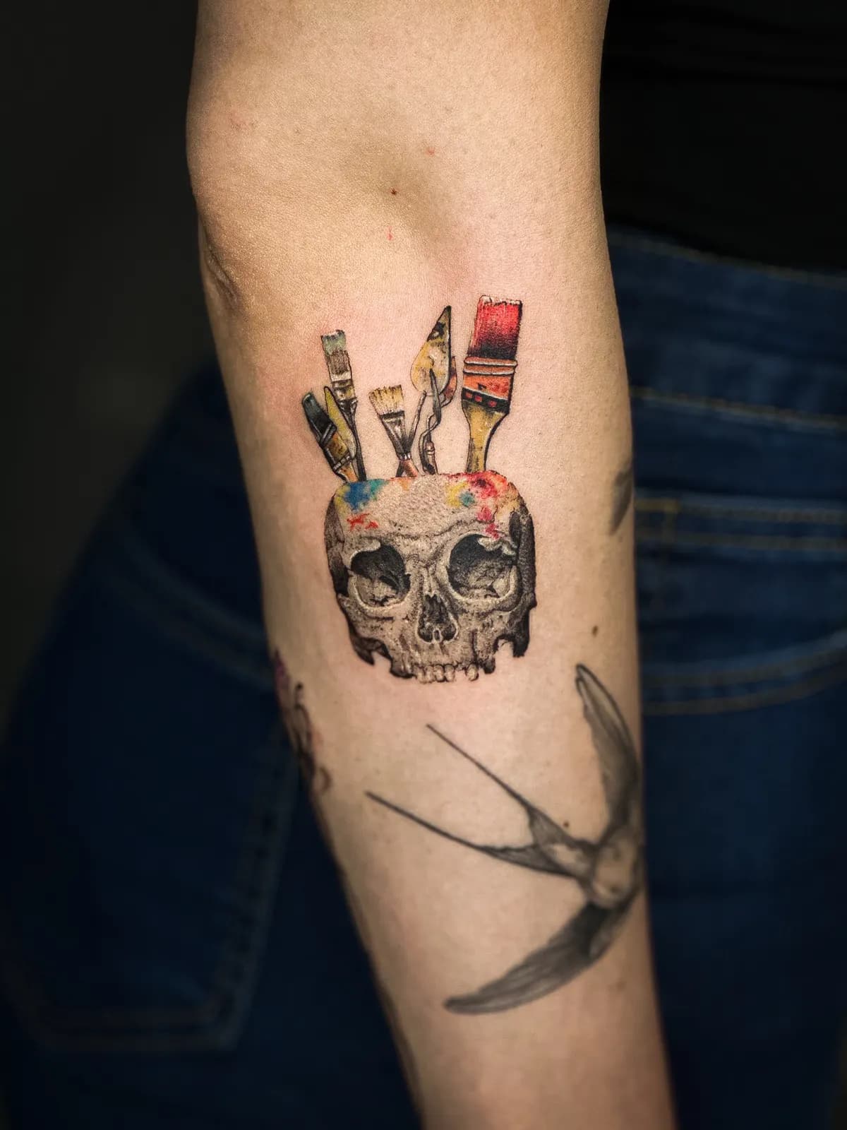 Tatuaj color pe braț cu un craniu din care ies pensule de pictor