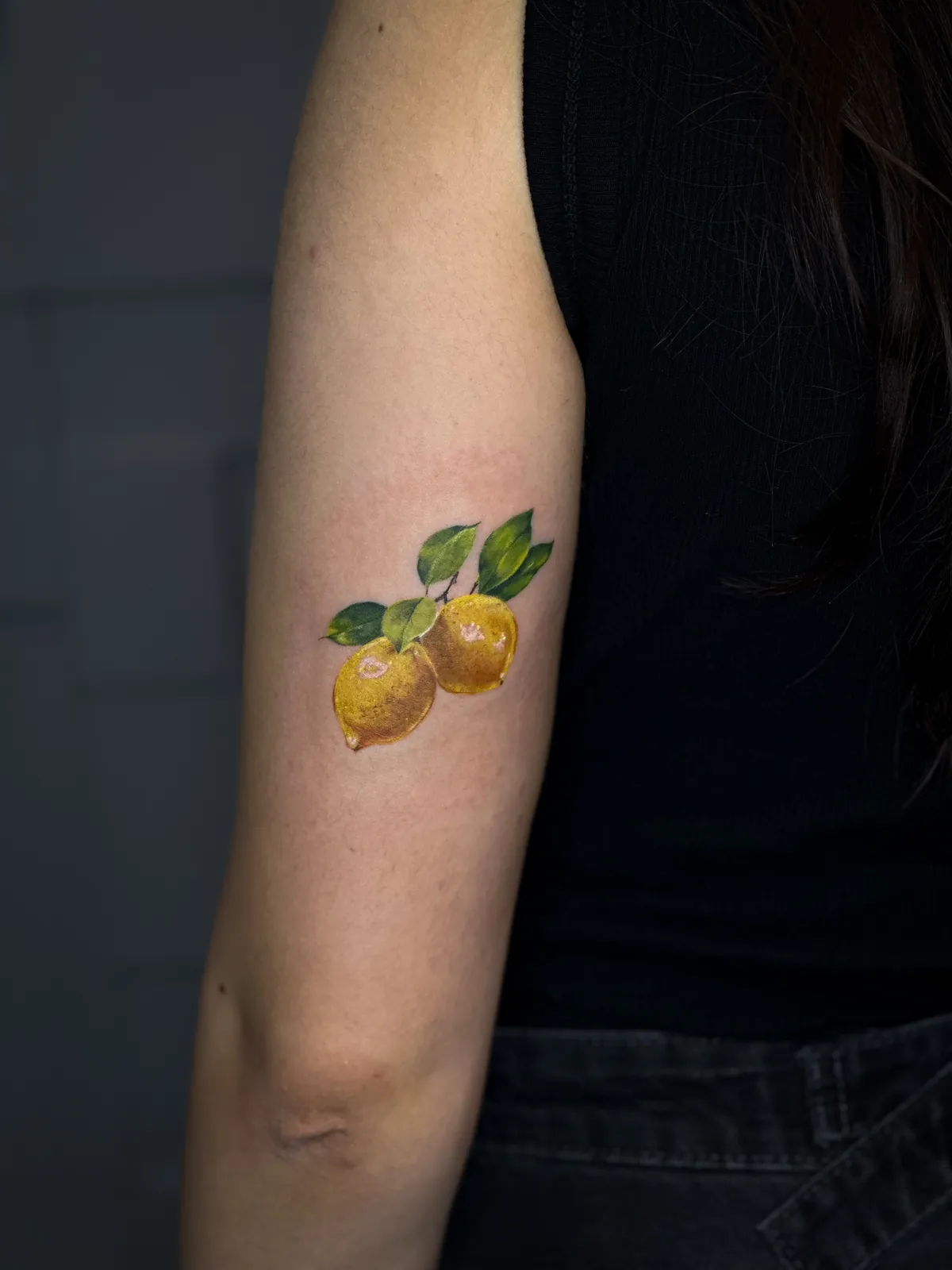 Tatuaj color realist pe braț cu două lămâi și frunze verzi