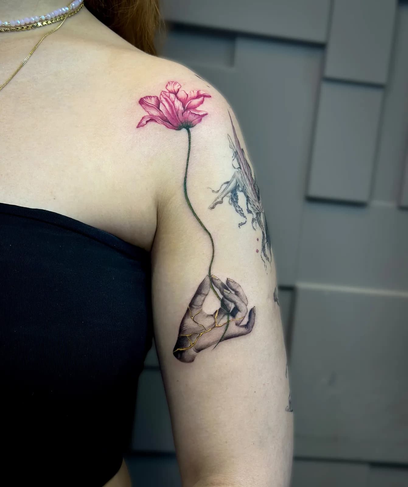 Tatuaj pe umăr și braț cu o floare de mac și o mână crăpată aurită în stil kintsugi