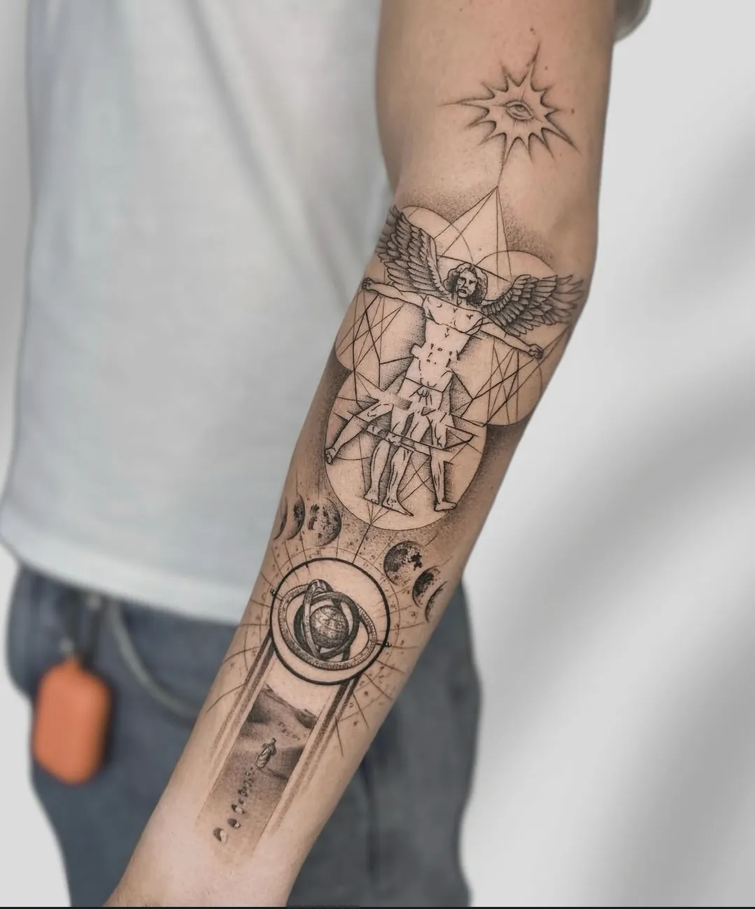 Tatuaj fine line pe antebraț cu omul vitruvian înaripat și un glob astronomic