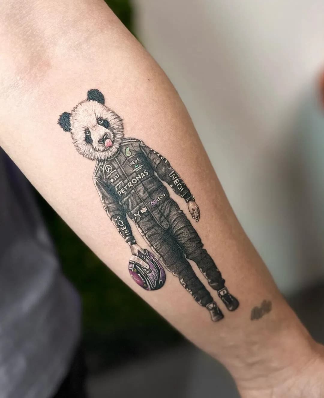 Tatuaj alb-negru pe antebraț cu un panda în costum de pilot de curse