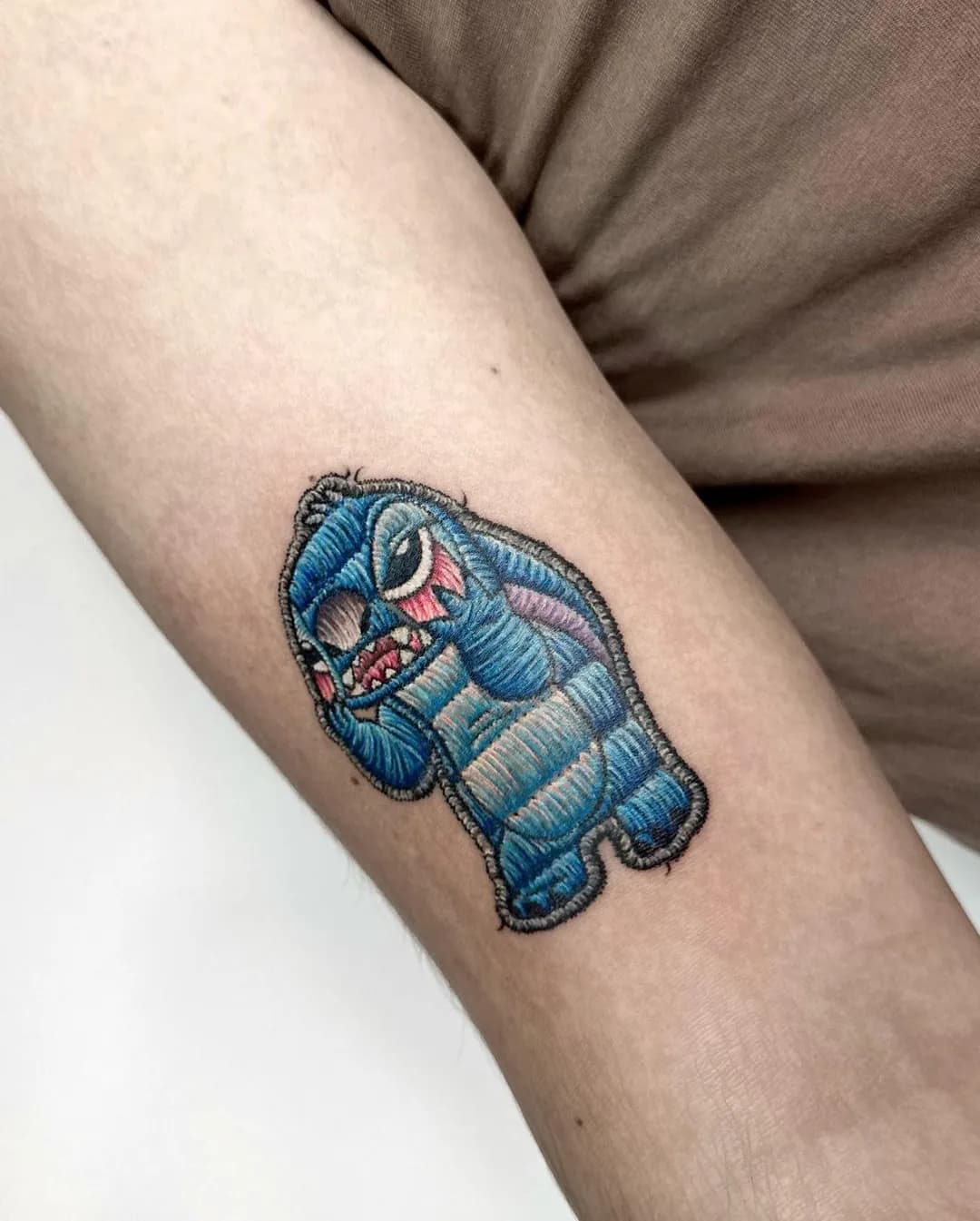 Tatuaj color pe braț cu un personaj albastru din desene animate