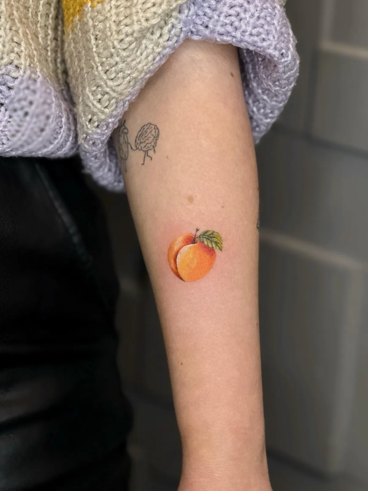 Tatuaj color realist pe braț cu o piersică tăiată în jumătate