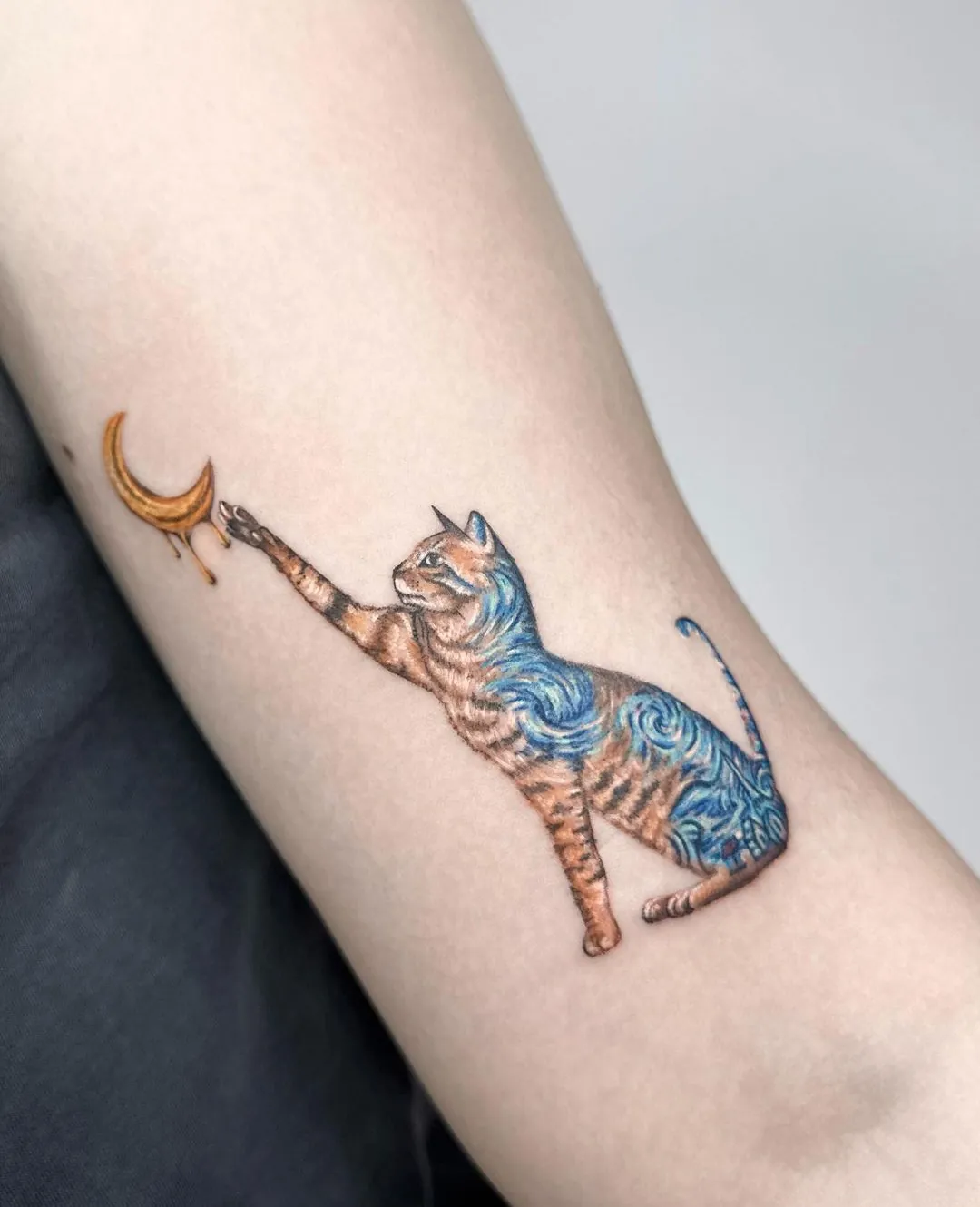 Tatuaj color pe braț cu o pisică ce atinge o semilună