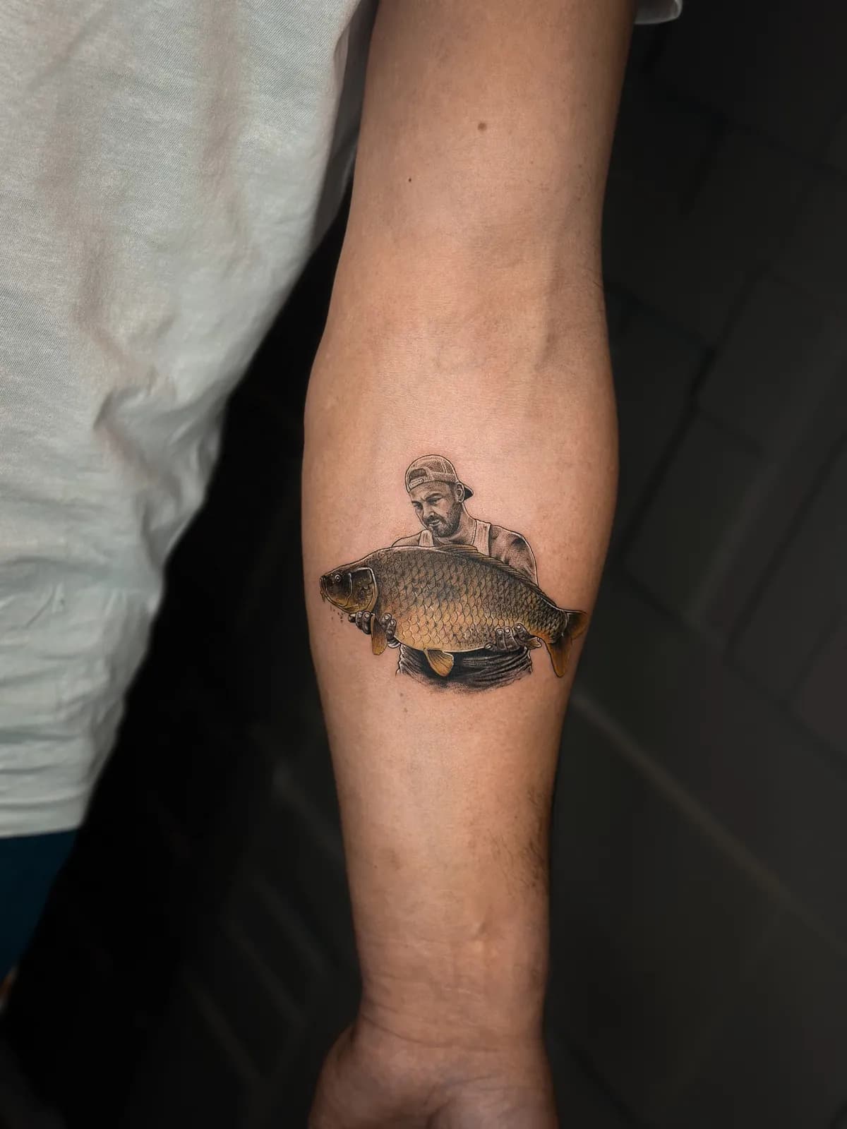 Tatuaj color realist pe braț cu un pescar ținând un crap mare