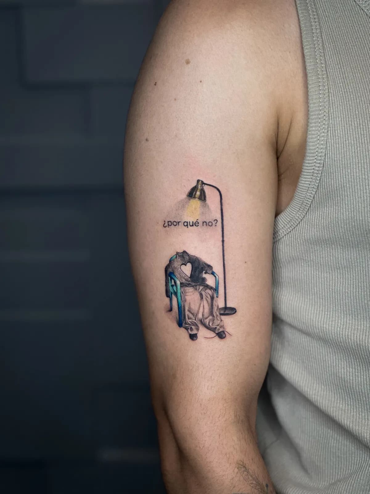 Tatuaj color pe braț cu un scaun, o geacă cu inimă decupată sub o lampă și textul ¿por qué no?