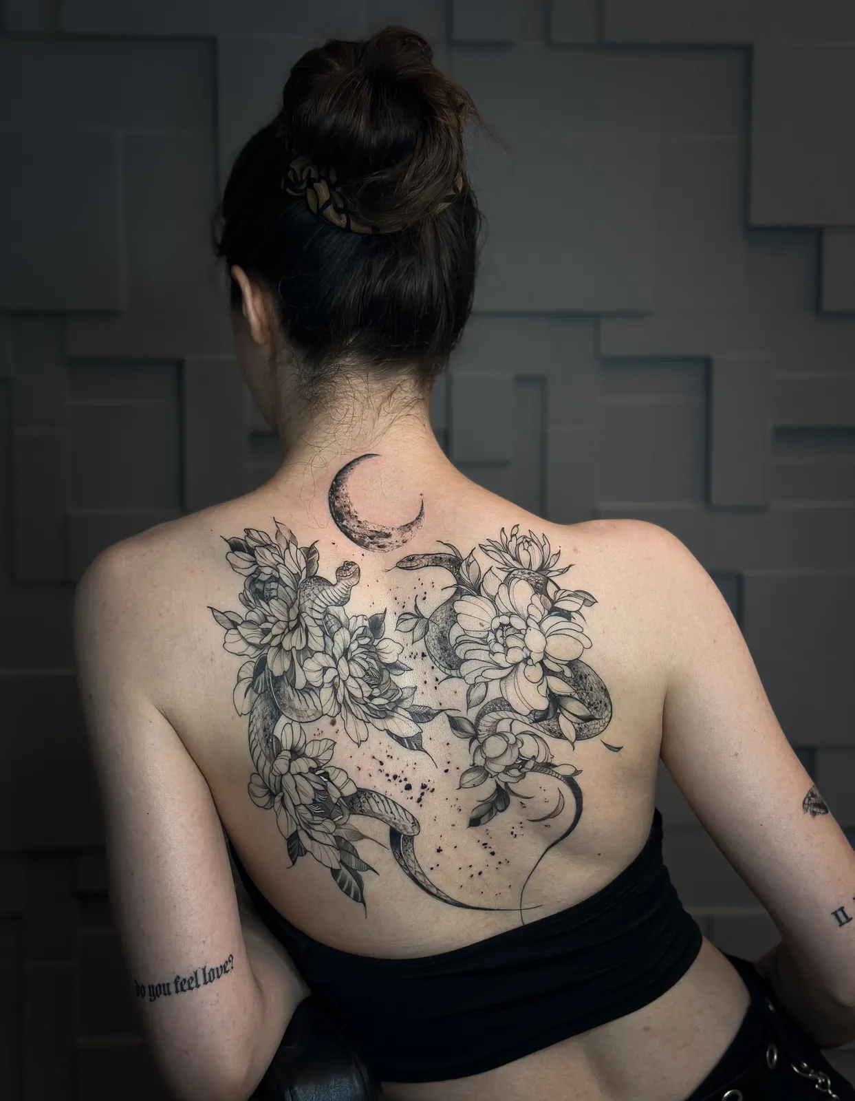 Tatuaj alb-negru pe spate cu doi șerpi printre bujori și o semilună la ceafă