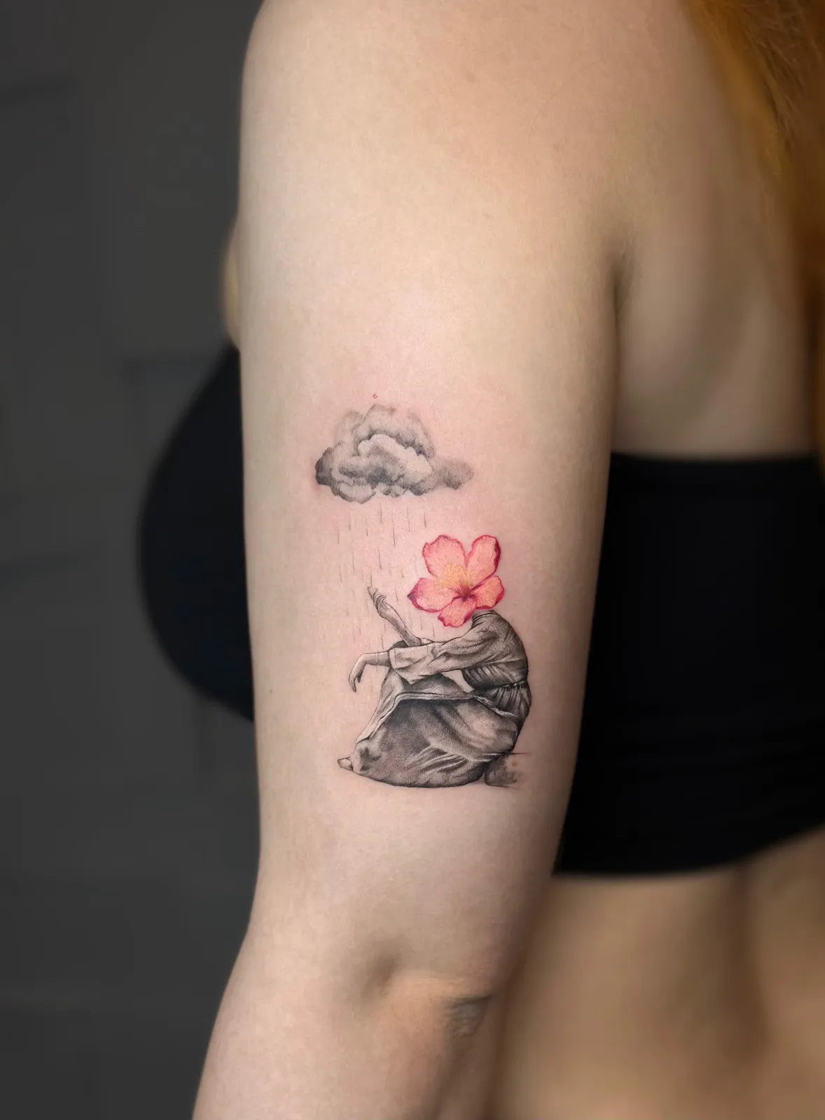 Tatuaj fine line pe braț cu o siluetă fără cap, cu cap de floare roz, sub un nor de ploaie