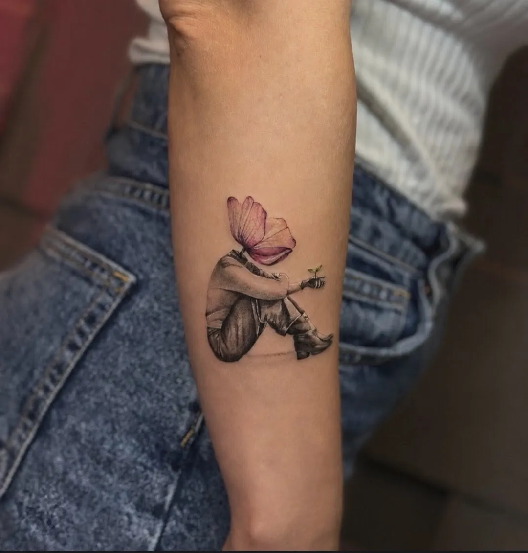 Tatuaj pe antebraț cu o siluetă așezată, cap de floare roz și un mugur în palmă